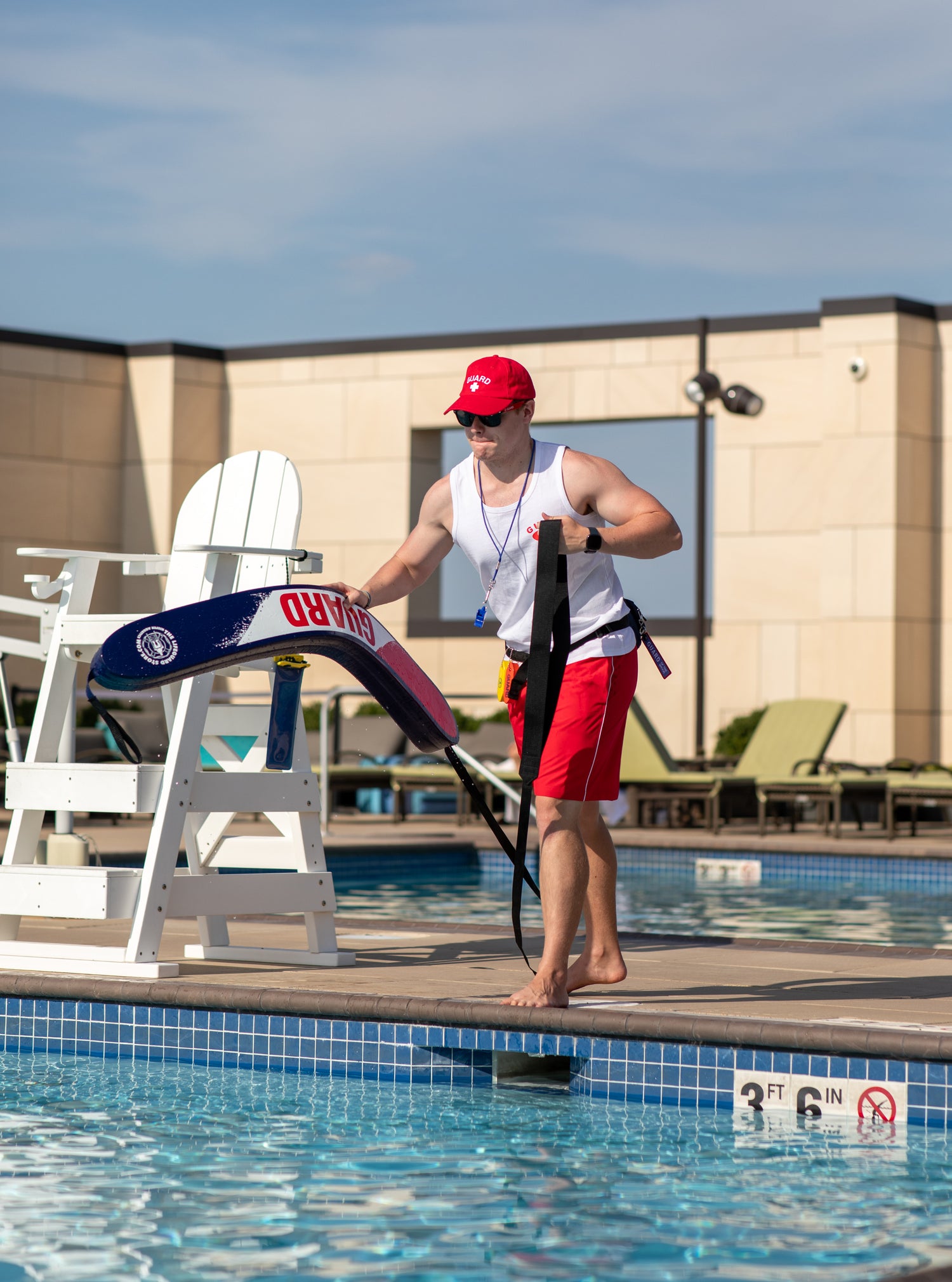 Man holding a surfboard by a pool with lounge chairs in the background